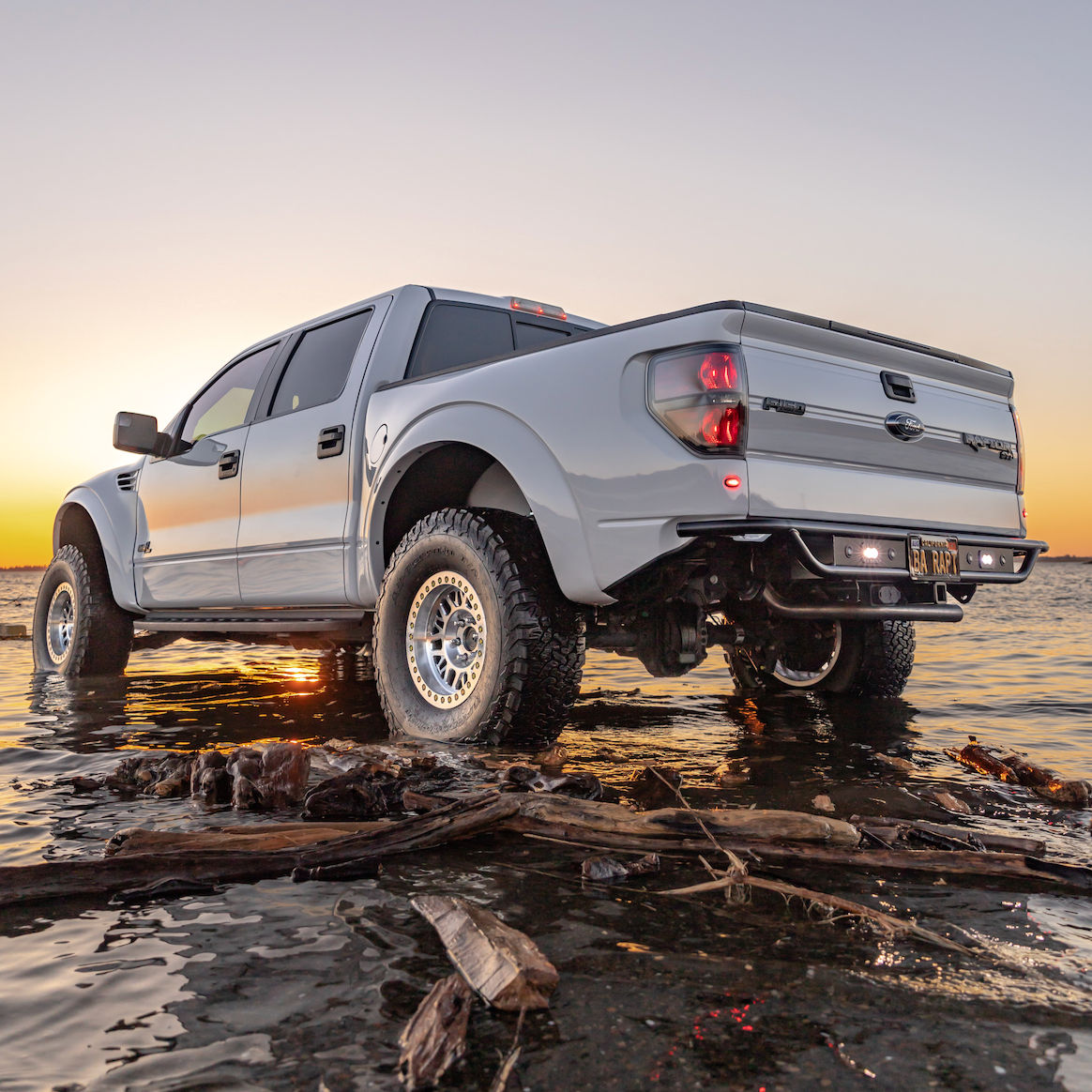 2010-2016 Ford Raptor bedsides showcased on a silver truck parked in shallow water at sunset.