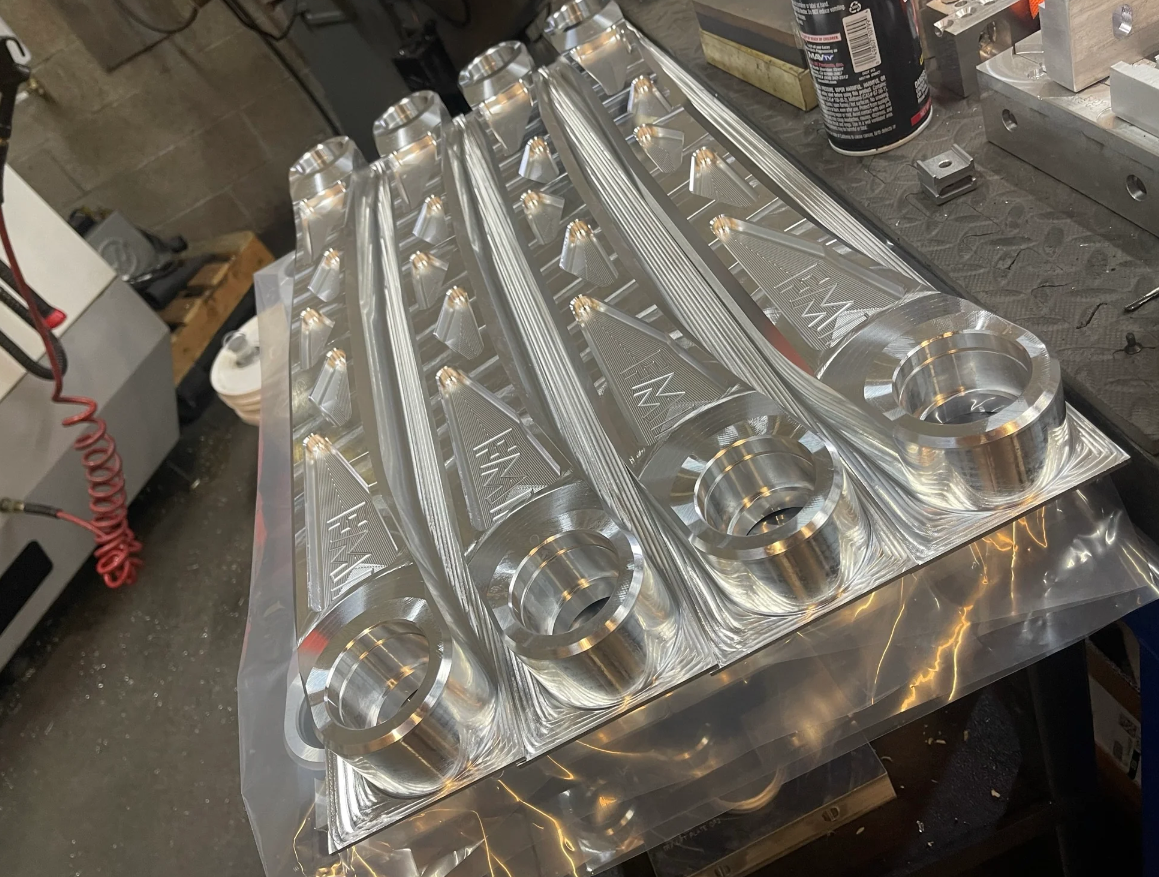 2021 and up Bronco rear suspension lower billet aluminum arms displayed on a workbench, showcasing precision engineering and design.