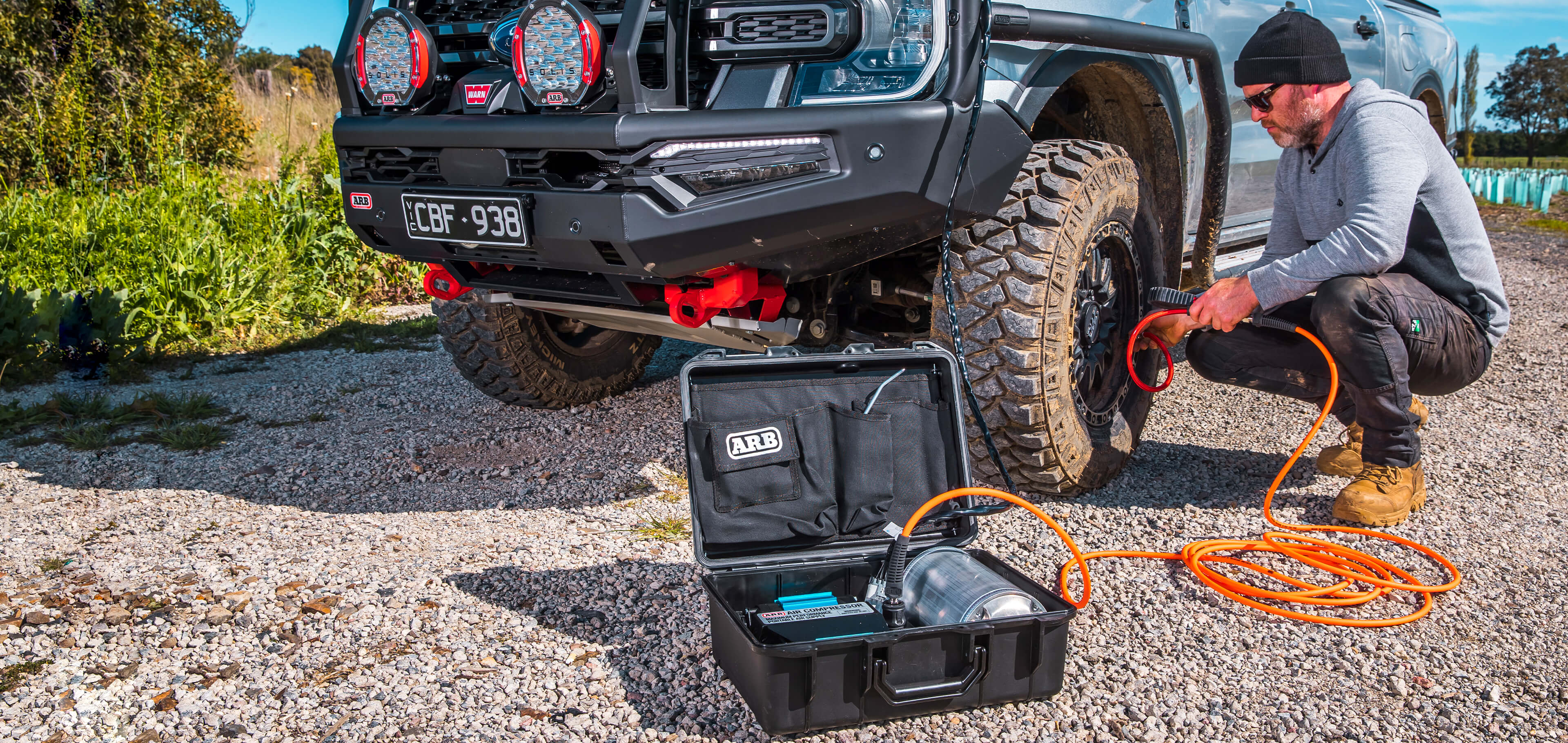 Man using an ARB Twin Compressor Package to inflate tires on an off-road vehicle in a natural setting.