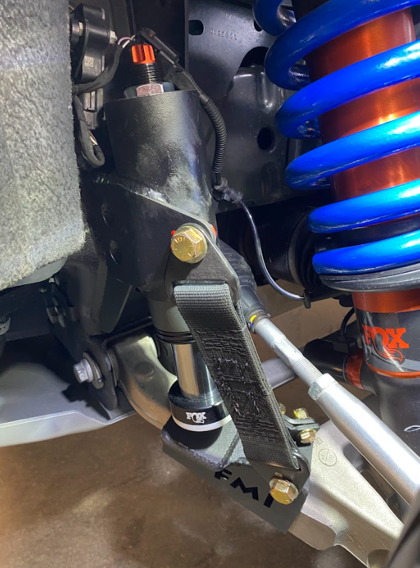 Front limit strap and bump stop installed on a 2022 Bronco Raptor's stock lower arm, showcasing suspension components.