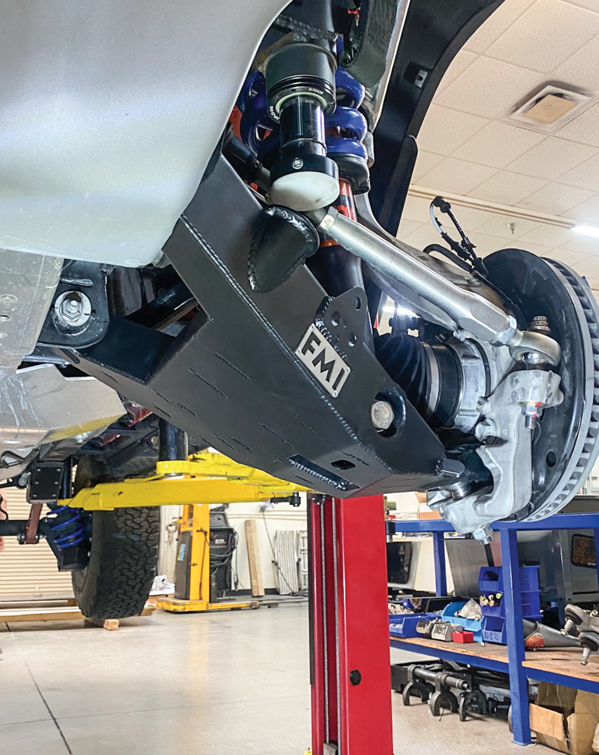 2022 Bronco Raptor mid travel front suspension kit installed, showcasing components and undercarriage details in a workshop setting.