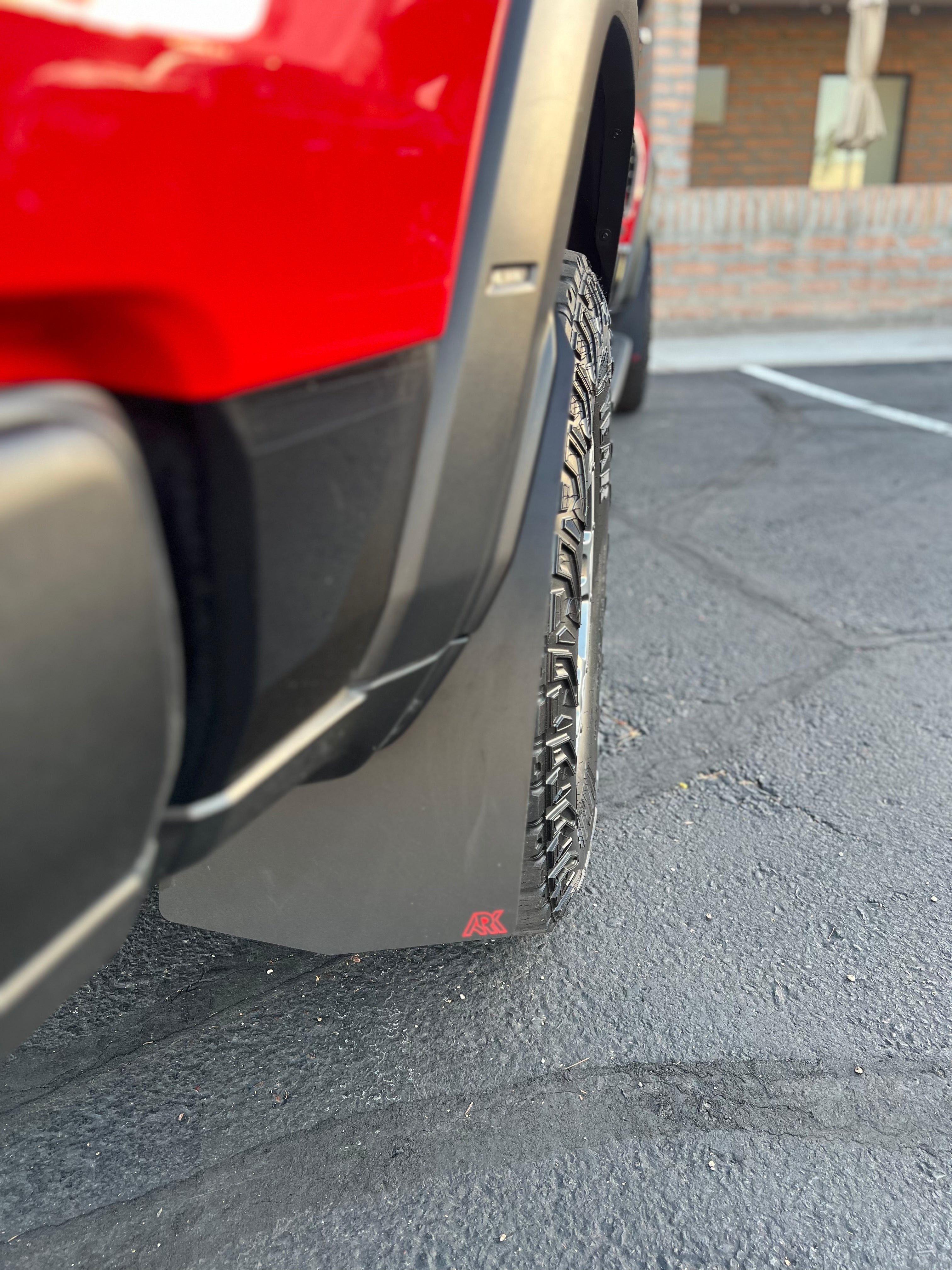 2025+ Dodge RAM RHO Mud Flaps installed on a truck, showcasing durable design and tire coverage on a paved surface.
