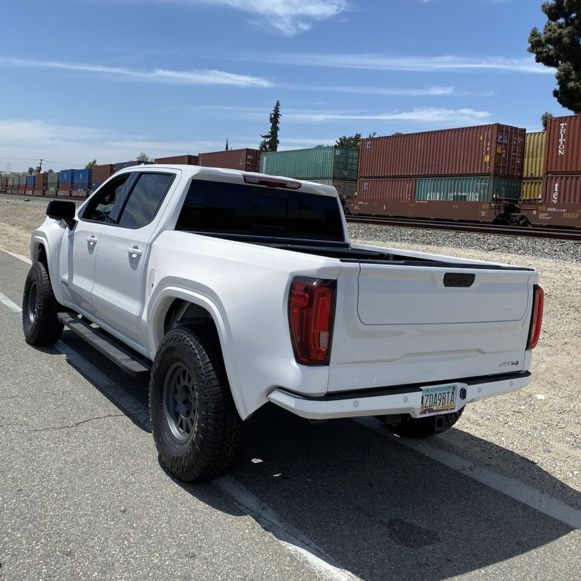2019-2025 GMC Sierra fenders installed on a modified white truck parked by a railway, showcasing offroad capabilities.