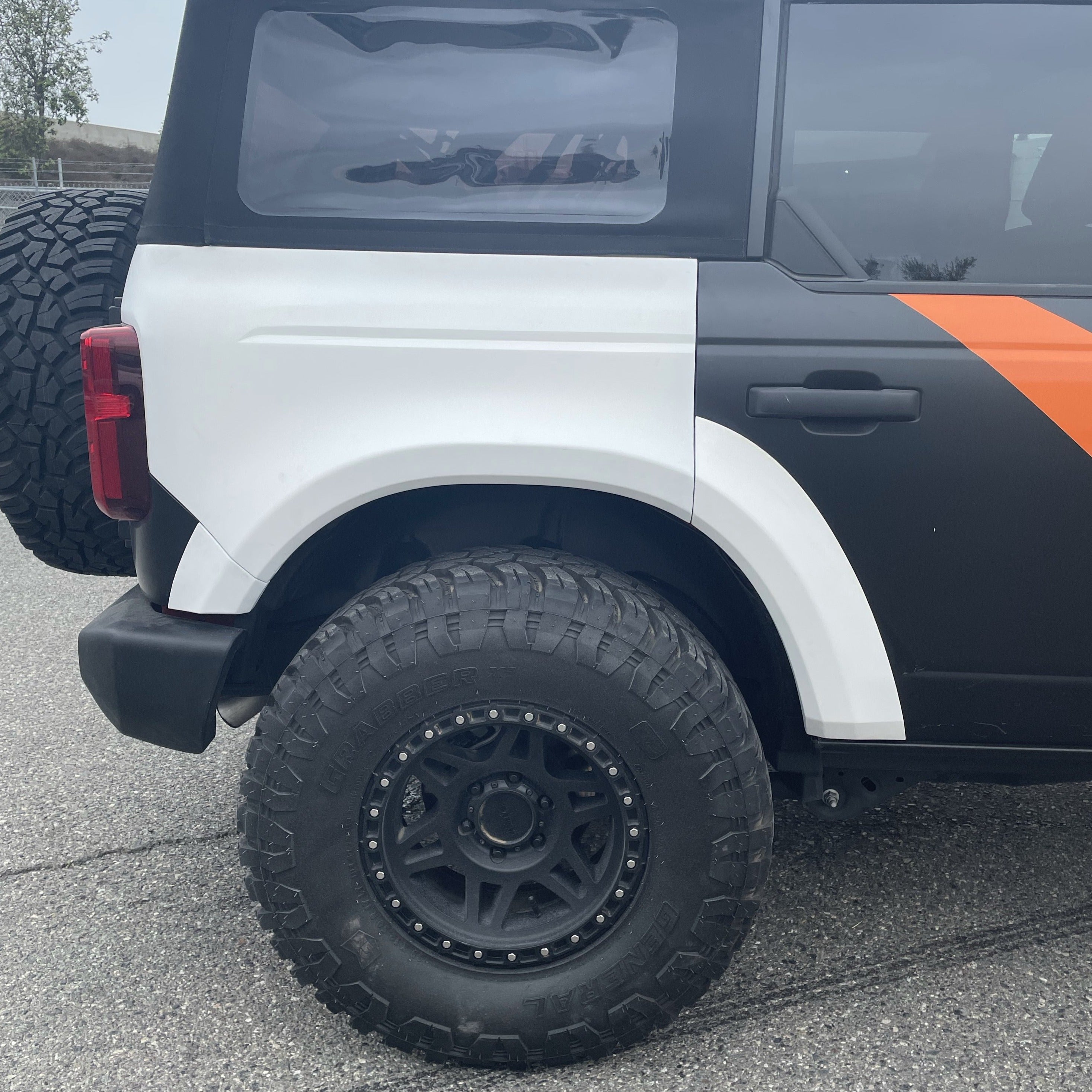 2021-2025 Ford Bronco 4-Door Rear Quarter Kit showcasing a rugged design with oversized tires and a sleek black and orange finish.