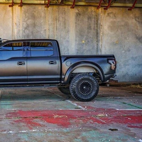2017-2020 Ford Raptor bedsides showcasing a rugged black truck with offroad tires in an industrial setting.