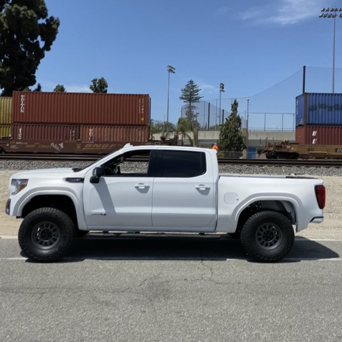 2019-2025 GMC Sierra fenders showcased on a lifted white truck parked beside shipping containers.