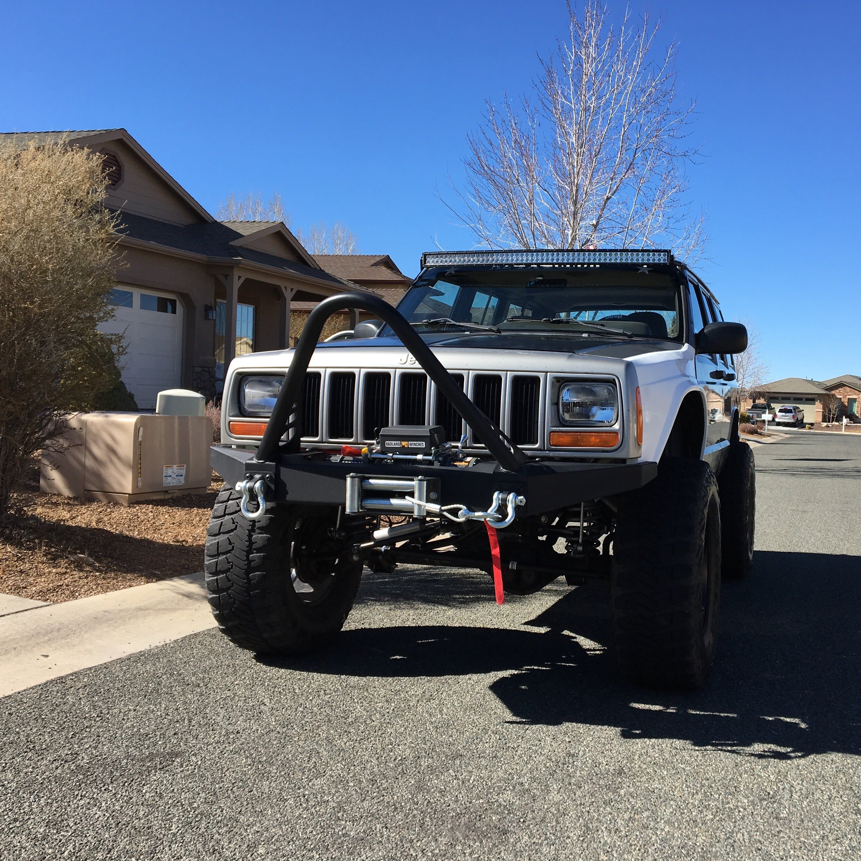 Front view of a lifted 1984-2001 Jeep Cherokee with aftermarket fenders and offroad accessories parked on a residential street.