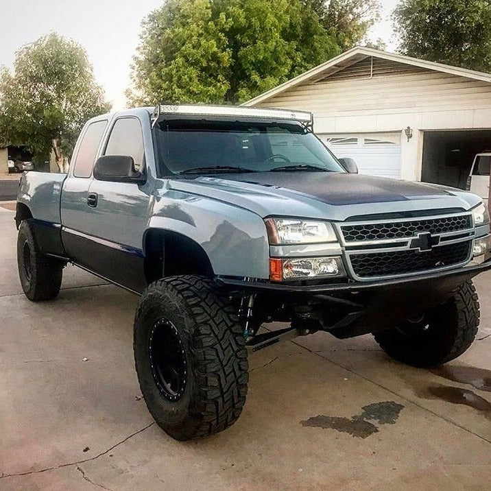 2003-2006 Chevrolet Silverado with aftermarket fenders and offroad tires parked in a driveway.