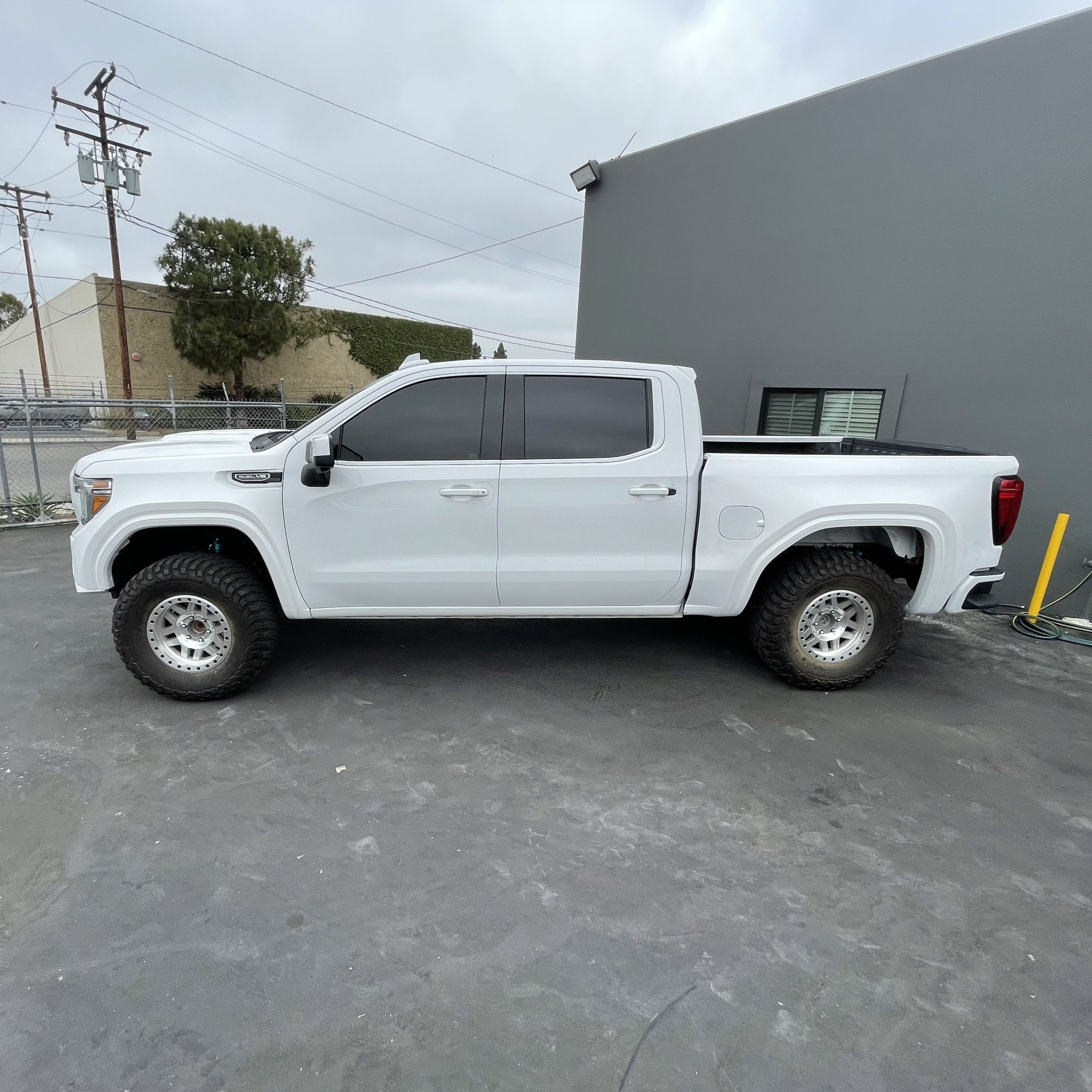 2019-2025 GMC Sierra with aftermarket bedsides, showcasing a lifted stance and off-road tires in a parking area.
