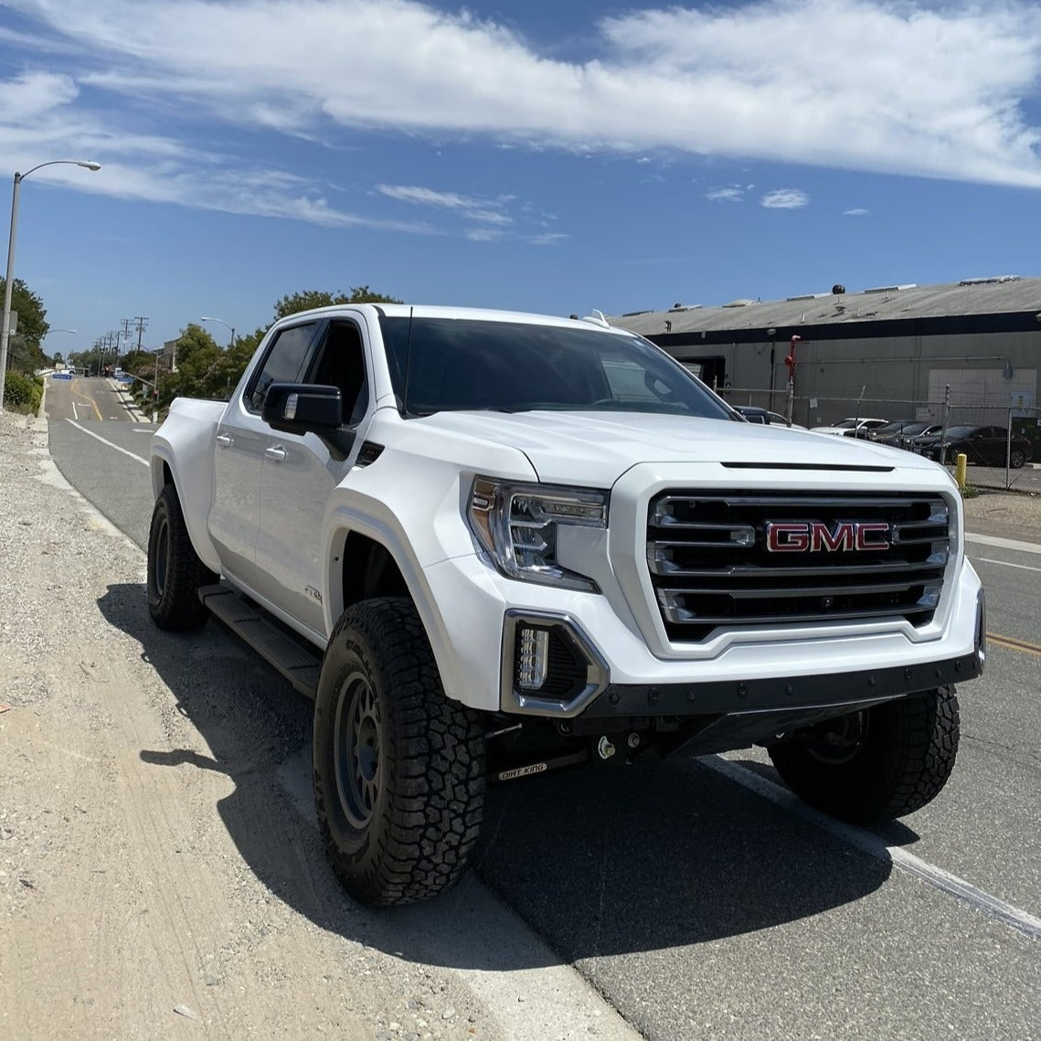 2019-2025 GMC Sierra fenders on a lifted white truck parked on a roadside, showcasing an offroad-ready design.