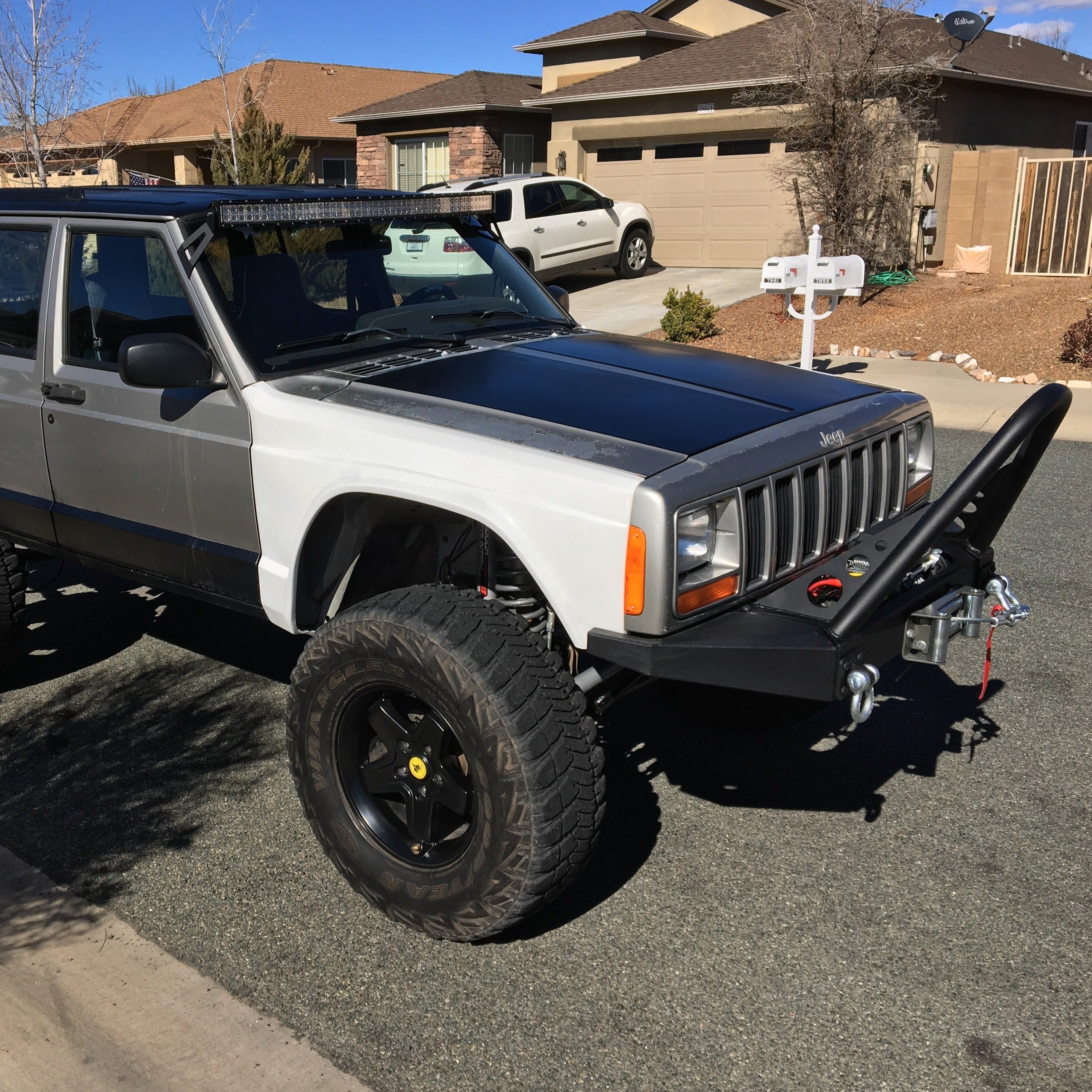 1984-2001 Jeep Cherokee with aftermarket fenders and offroad modifications parked on a residential street.