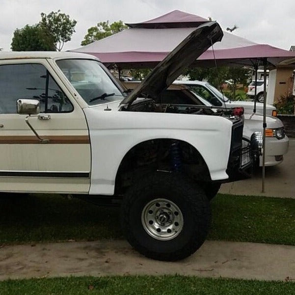 1980-1986 Ford Bronco with open hood showcasing aftermarket fenders and offroad tires in a residential setting.