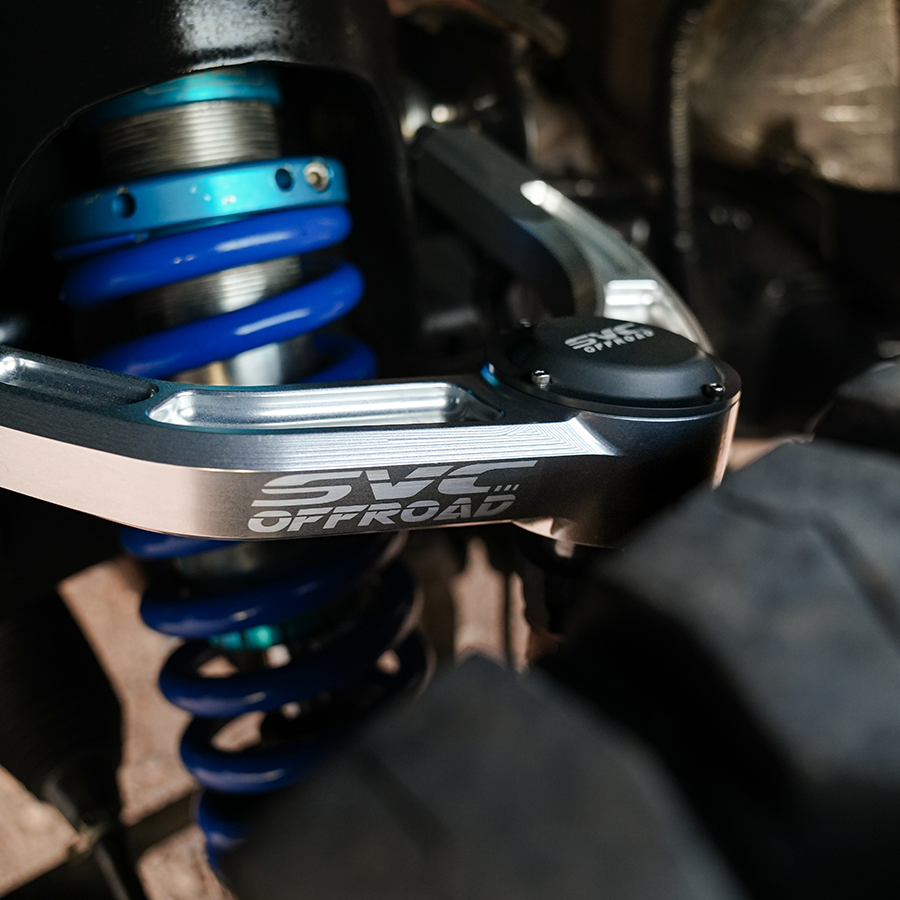 2021+ Raptor upper control arms showcasing durable aluminum construction and blue coil spring for enhanced offroad performance.
