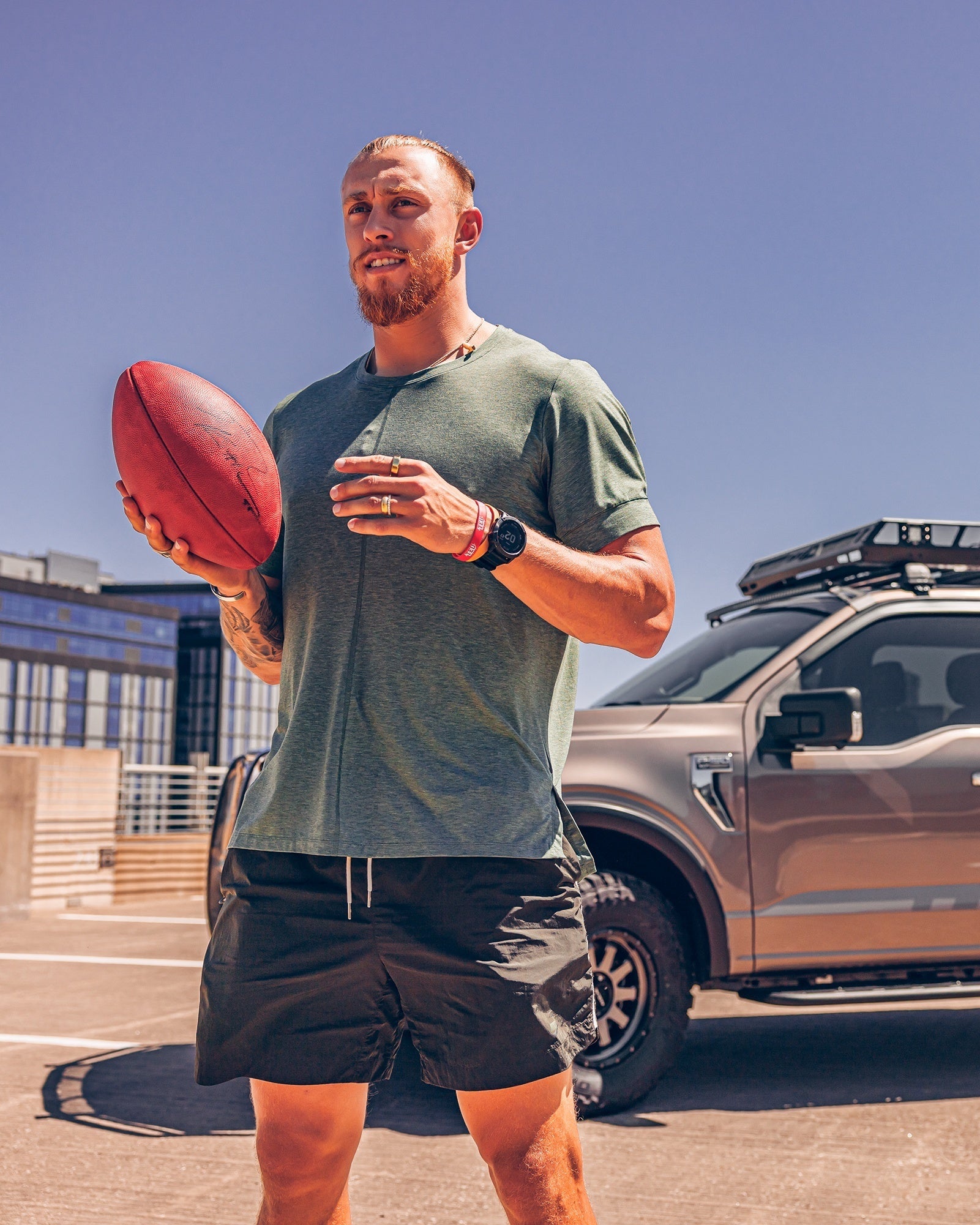 Athlete holding a football outdoors near a truck, showcasing a sporty lifestyle and rugged vehicle.