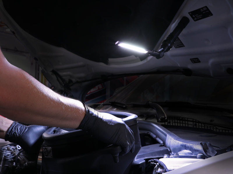 aFe Magnetic Folding Flashlight illuminating an engine bay, with a hand in gloves working on a vehicle part.