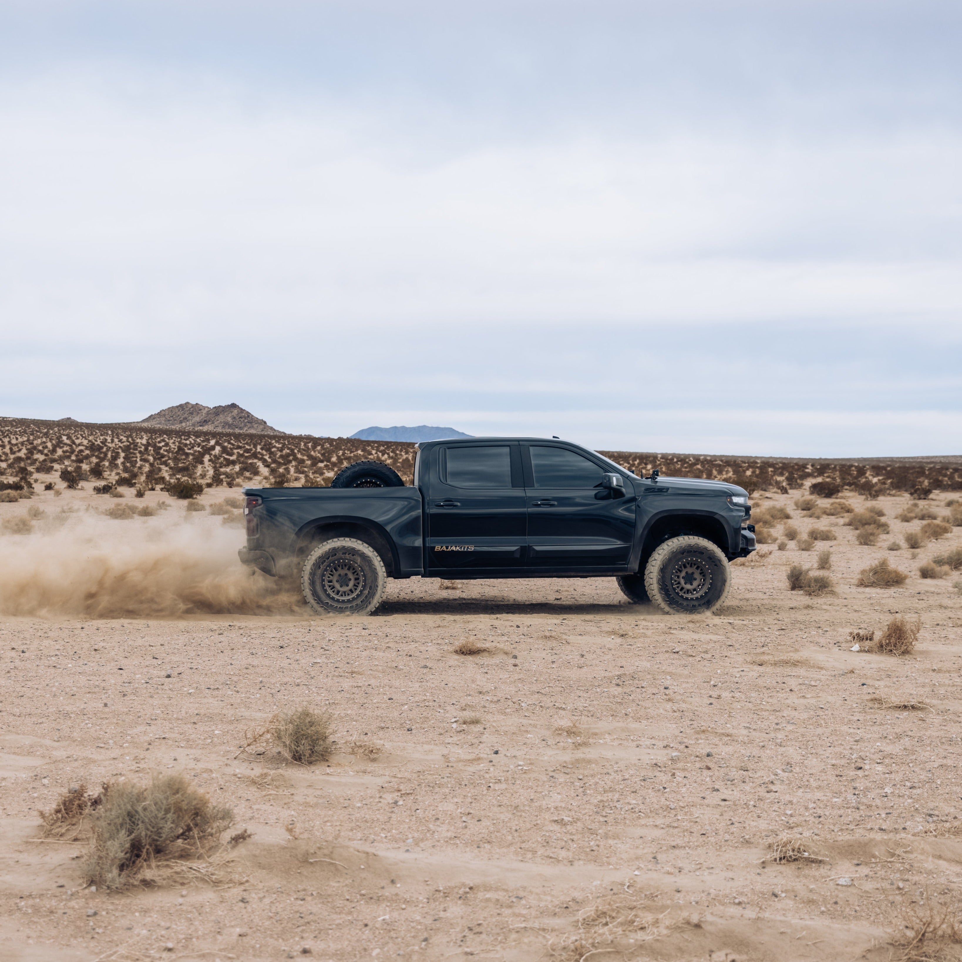 2019-2021 Chevrolet Silverado with aftermarket bedsides driving through a desert landscape, kicking up dust.