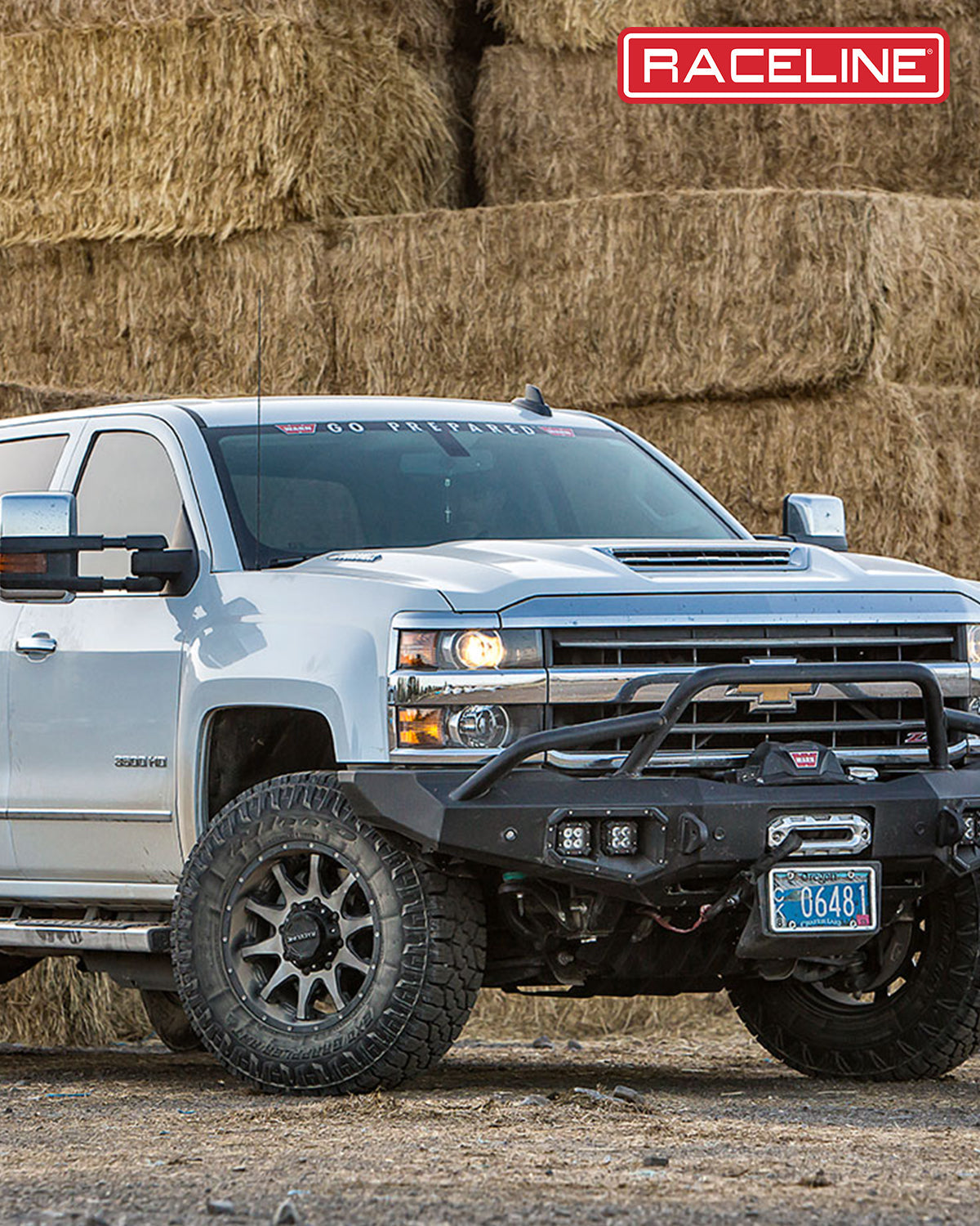 Chevrolet truck with a custom front bumper and off-road tires parked near hay bales, showcasing rugged design and performance.