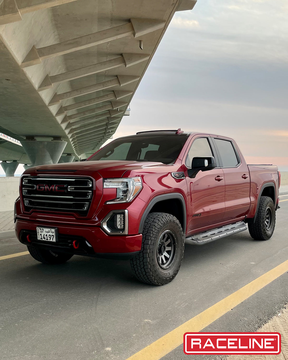 Red GMC truck parked under a bridge, showcasing rugged off-road tires and a sleek design, ideal for off-road enthusiasts.