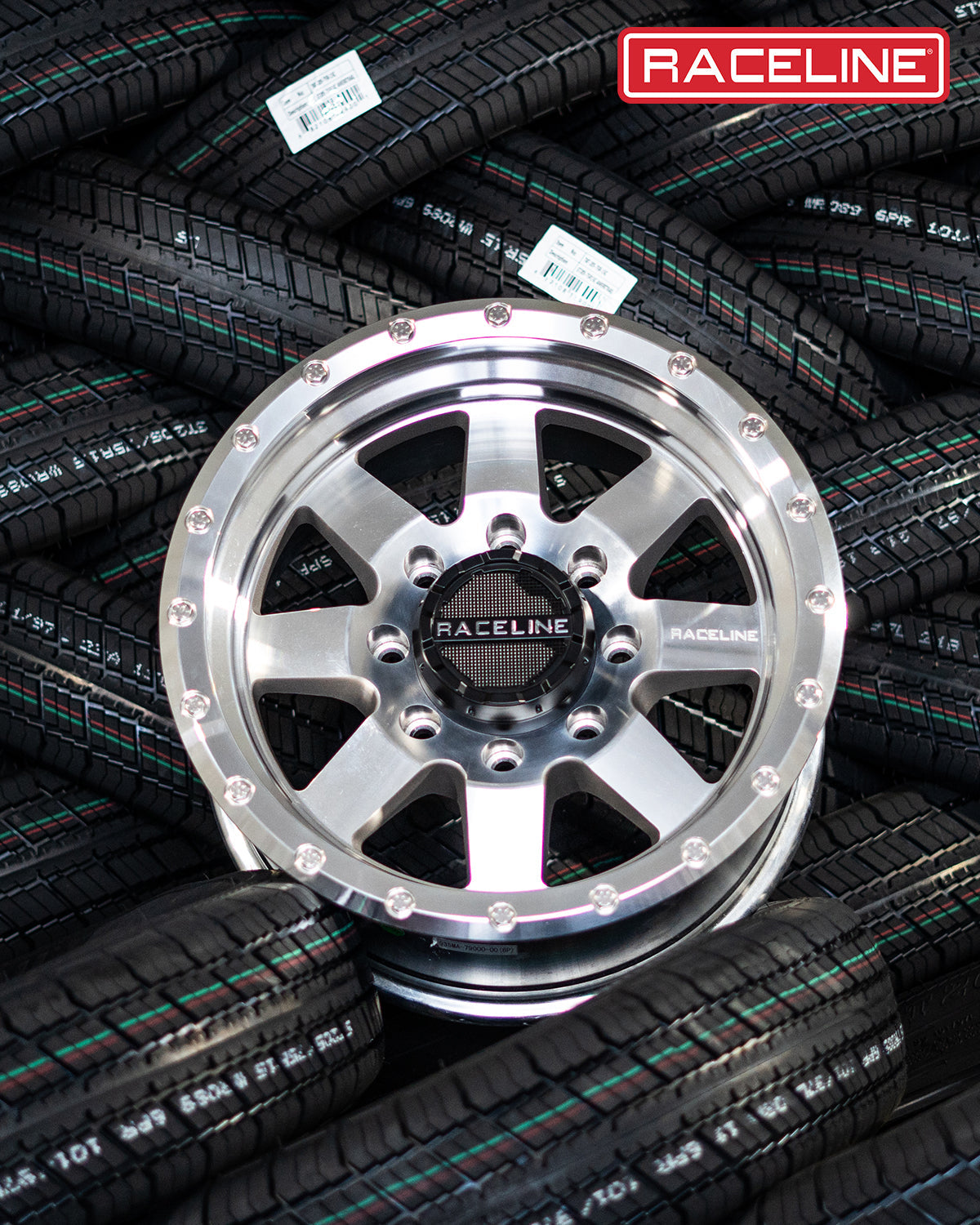 Aluminum 935MC Defender wheel by Raceline, showcased on a background of stacked offroad tires.