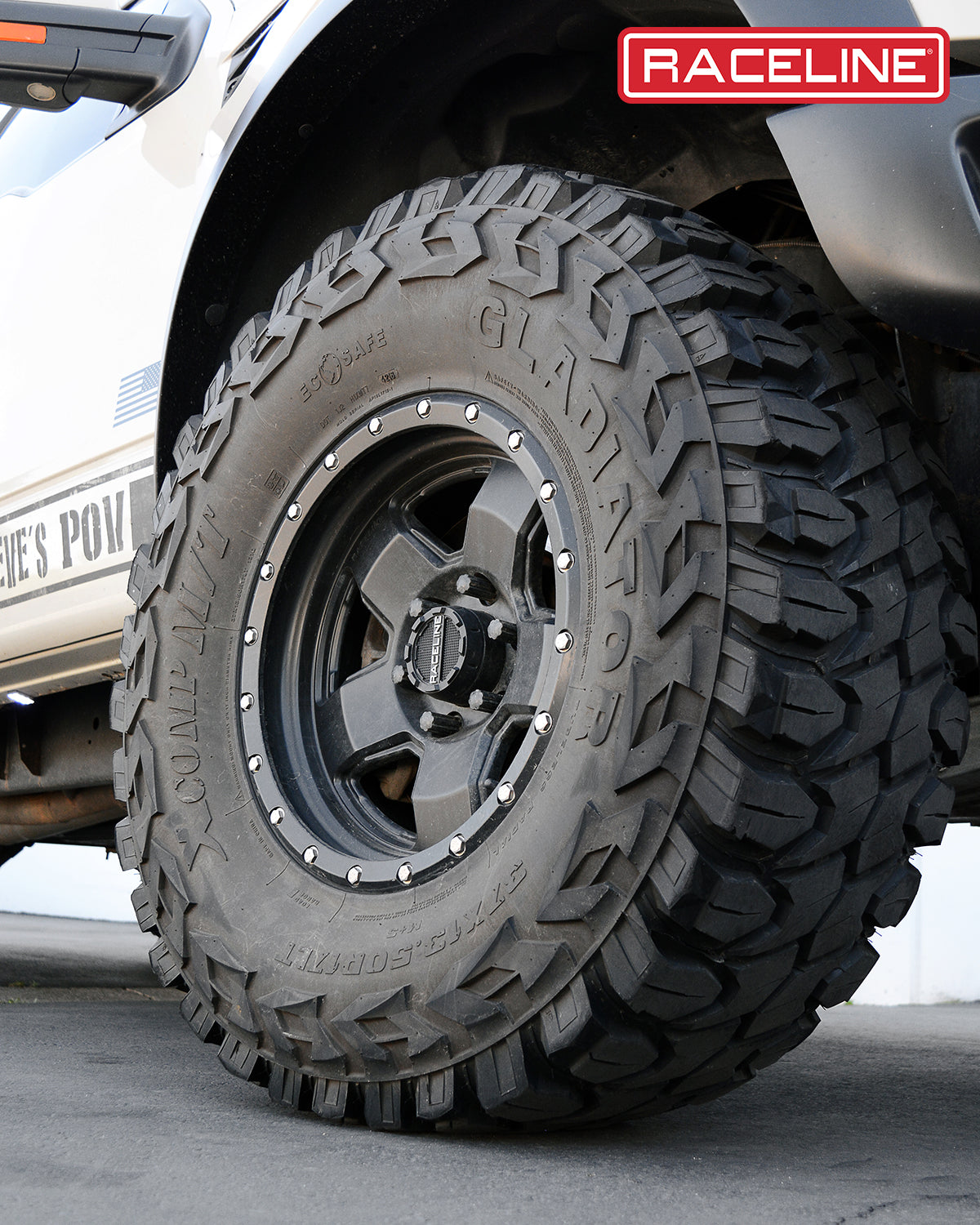 Close-up of a Raceline 937B Combat wheel mounted on a rugged tire, showcasing its aggressive tread design and black finish.