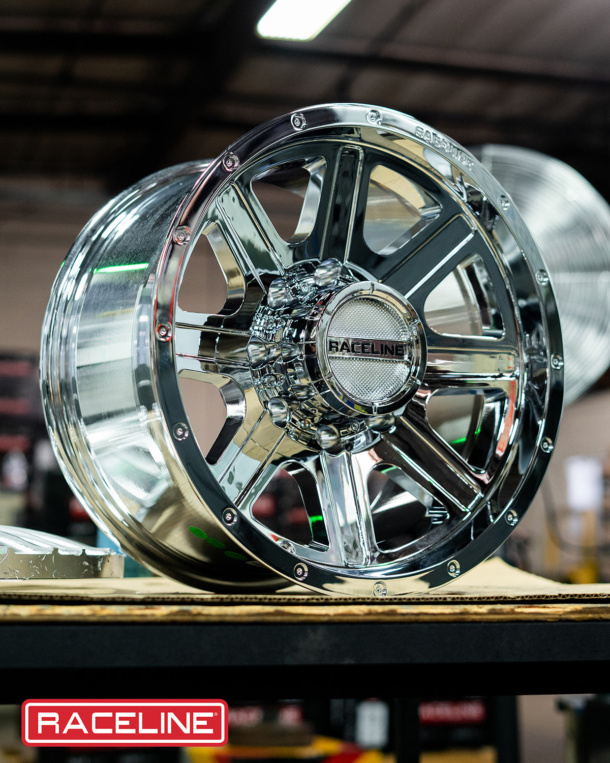 Shiny Raceline 940C Hostage wheel displayed on a workbench, showcasing its polished chrome finish and intricate design.