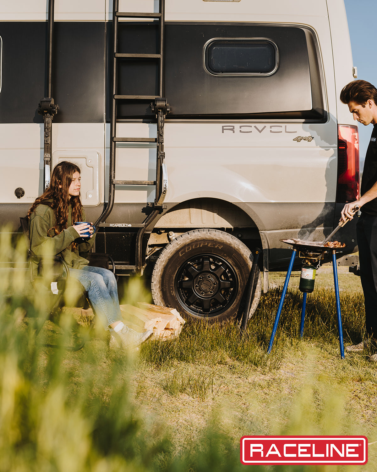 A person cooking outdoors near a 947B Scout Van, showcasing its rugged design and offroad capabilities.