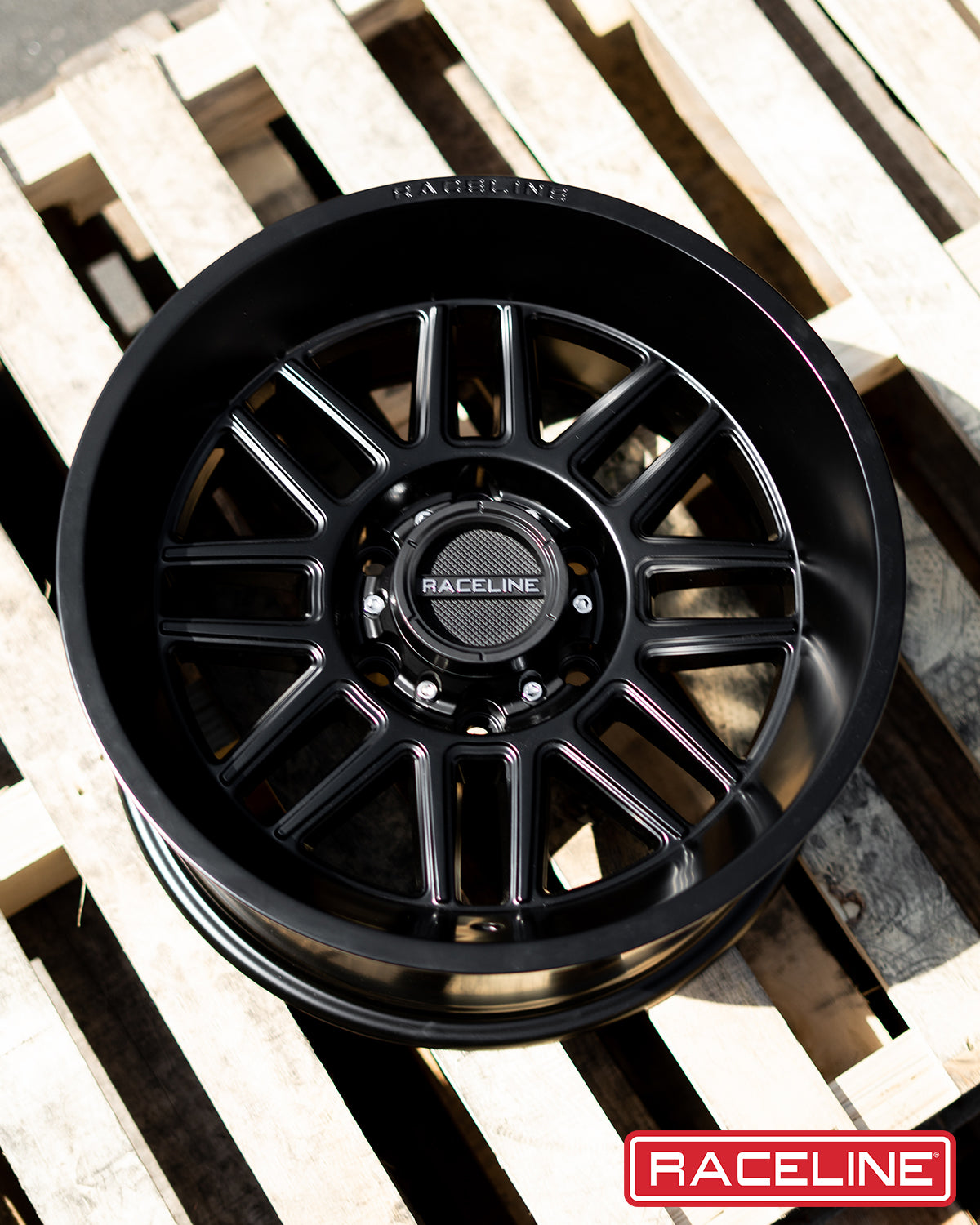 Black Raceline 948B Split wheel displayed on wooden pallets, showcasing its sleek design and polished finish.