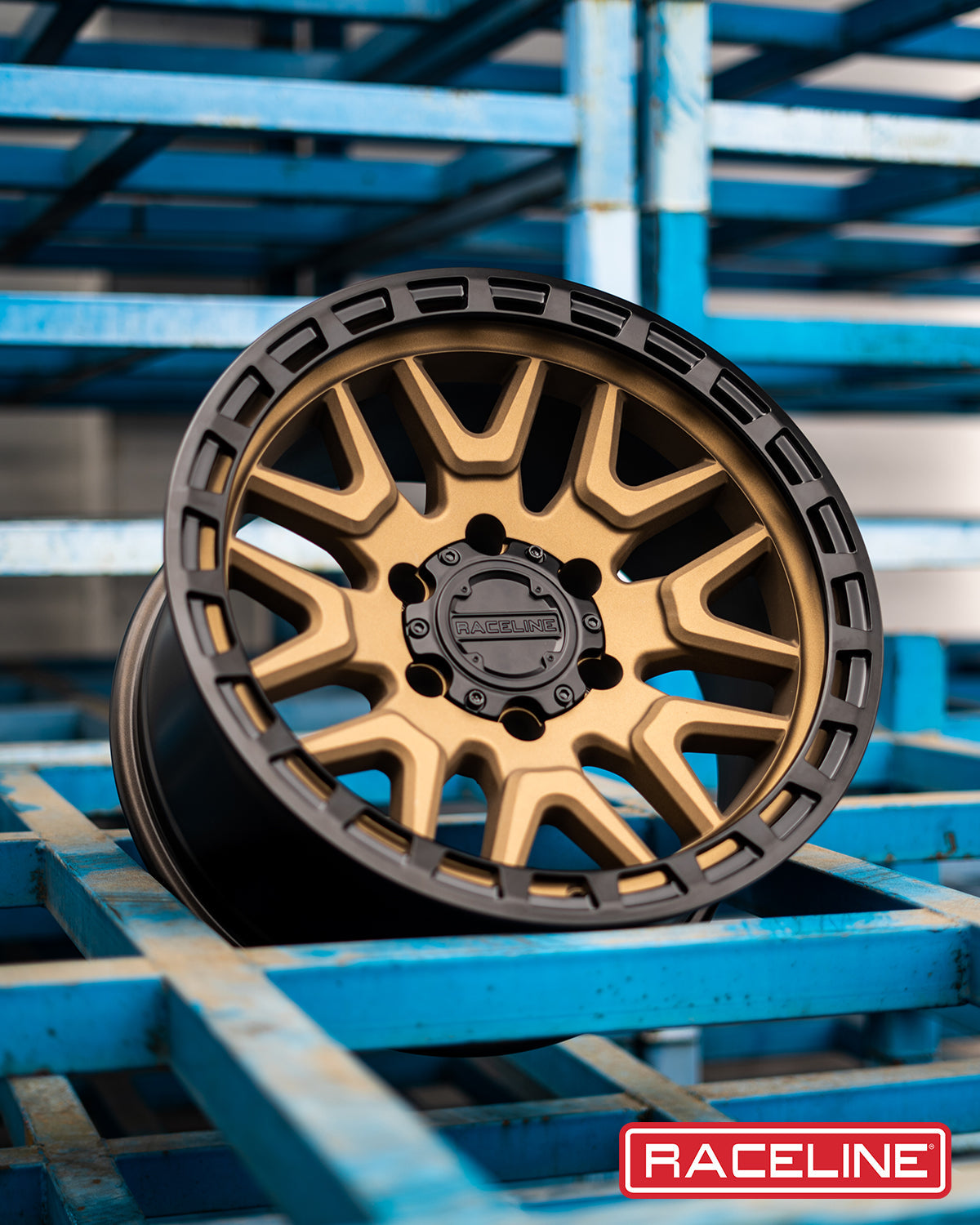 Stylish Raceline 953BZ Krank wheel featuring a gold and black finish, displayed on a blue storage rack.
