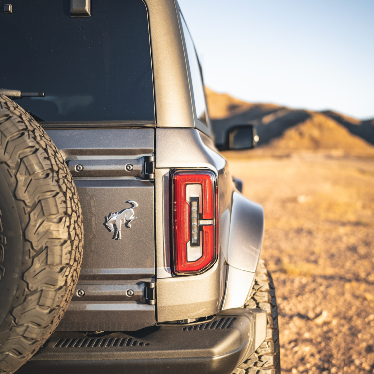 2021-2024 Ford Bronco 4-Door Rear Quarter Kit showcasing the vehicle's rear design and tire mount in a rugged landscape.