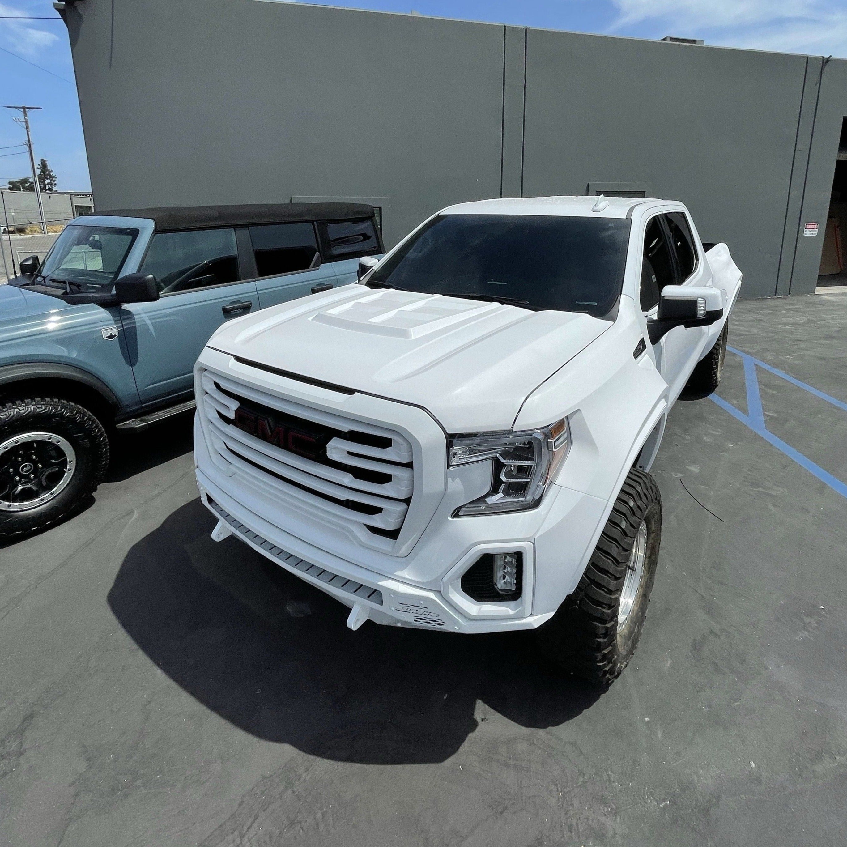 2019-2021 GMC Sierra hood displayed on a lifted white truck, showcasing its aggressive design and offroad capabilities.