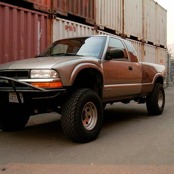 1994-2005 Chevrolet S-10 with lifted suspension and offroad tires, parked in front of shipping containers.